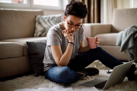 Woman drinking coffee and looking at laptop.